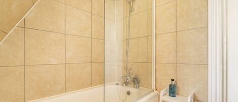 A bathroom with a bathtub, shower, and a small shelf with a bottle.