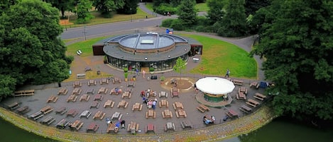 A circular outdoor area with wooden benches and a central circular structure, surrounded by trees and a body of water.