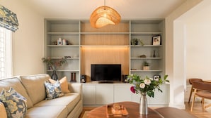 Una sala de estar con sofá, televisor, mesa de centro de madera y estantes con adornos.