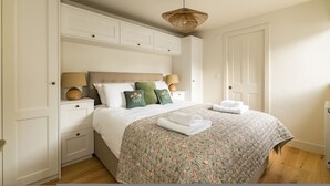 Un dormitorio con cama, mesitas de noche, una lámpara colgante y una puerta.