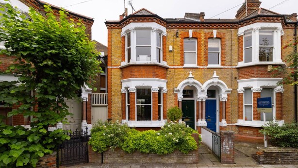 A two-story brick house with bay windows, a green door, and a white picket fence. - Battersea Park 3 Bedroom House With Private Garden (London)