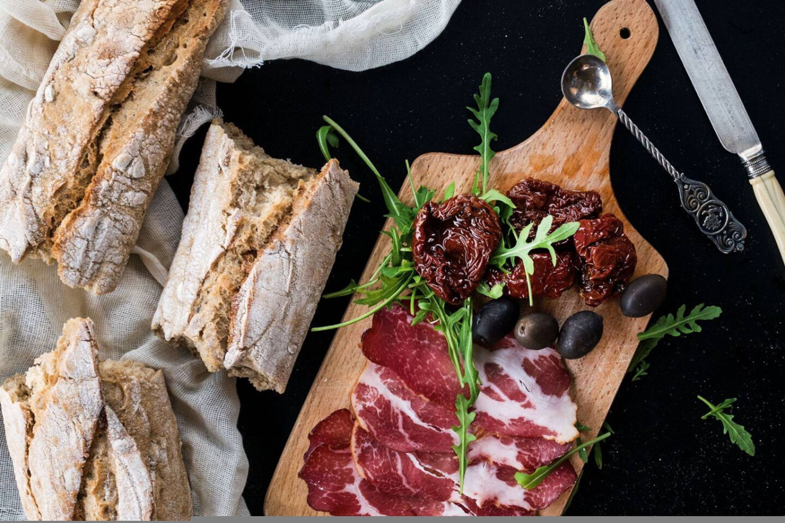 Una tabla de madera con carnes cortadas, aceitunas y frutas secas, acompañada de pan rústico.