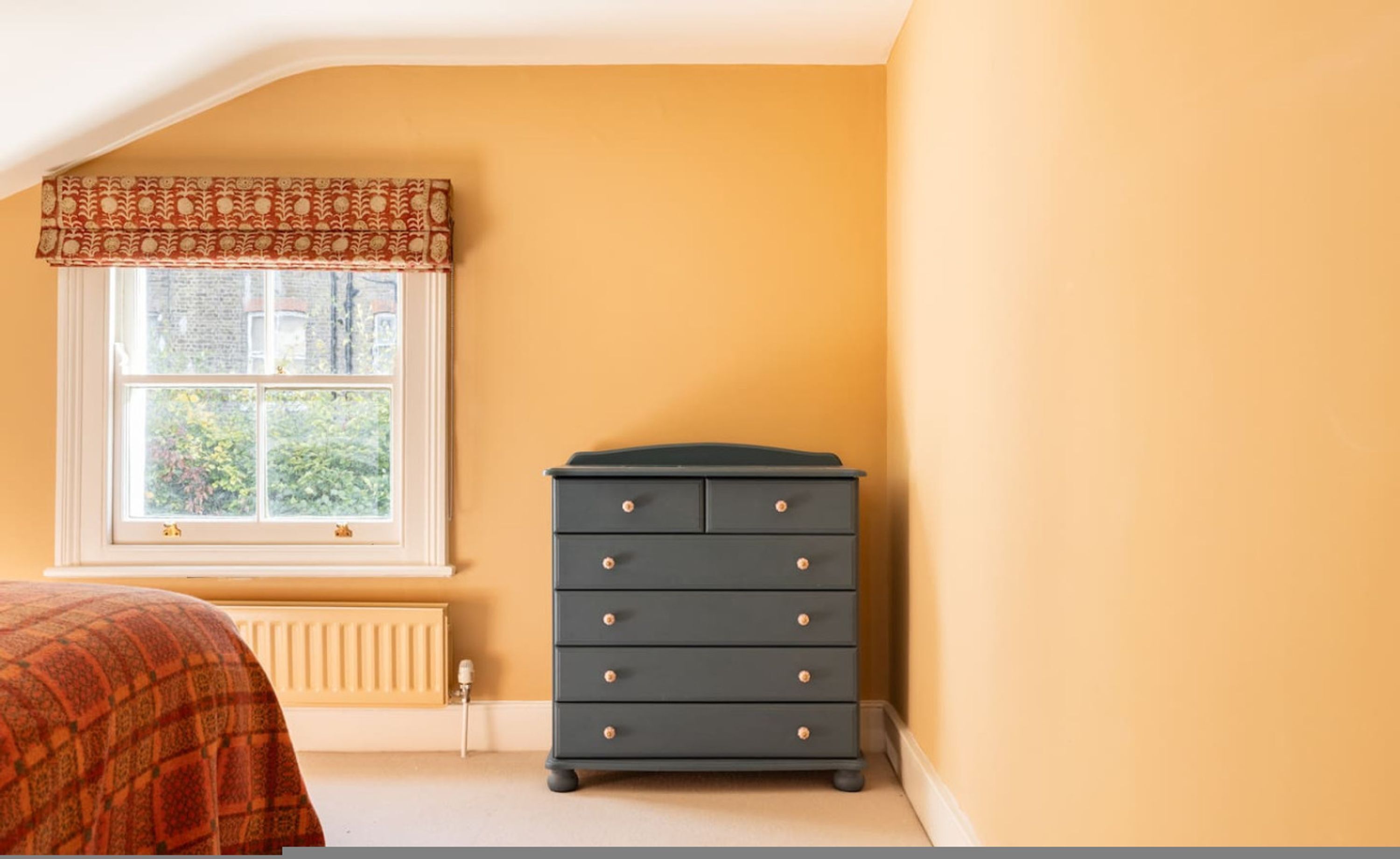 Ein Schlafzimmer mit Fenster, Heizkörper, Bett und Kommode.