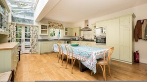A spacious kitchen with a dining table, wooden chairs, a large window, and a skylight. - Battersea Park 3 Bedroom House With Private Garden (London)