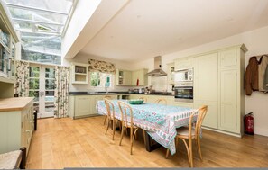A spacious kitchen with a dining table, wooden chairs, a large window, and a skylight. - Battersea Park 3 Bedroom House With Private Garden (London)