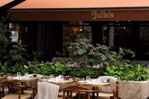An outdoor seating area with tables and chairs, a sign reading 'Julie's', and lush greenery. - Your Zen - 2 Bedroom Mews House in Notting Hill (London)