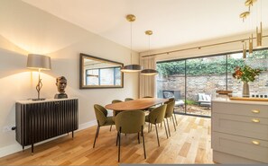 A modern kitchen with a dining area, a radiator, and a view of the garden. - Your Zen - 2 Bedroom Mews House in Notting Hill (London)