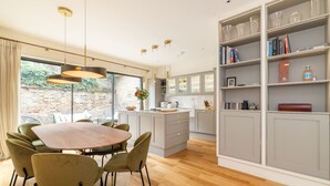 Een moderne keuken met grijze kastjes, een eettafel met stoelen en een groot raam met gordijnen.