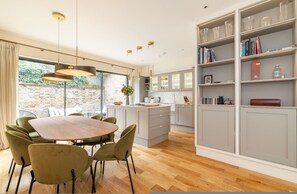 A modern kitchen with grey cabinets, a dining table with chairs, and a large window with curtains. - Your Zen - 2 Bedroom Mews House in Notting Hill (London)