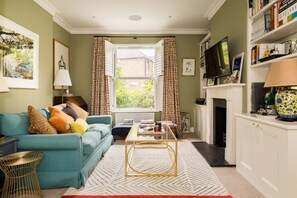 Ein Wohnzimmer mit Sofa, Couchtisch, offenem Fenster, Kamin und Bücherregal.