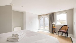 A hotel room with a bed, a chair, a lamp, a window, and a door. - The Thames Embrace 3 BR Garden House in Battersea (London)