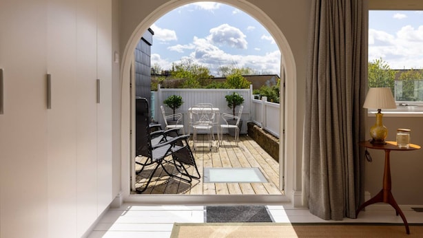 An arched doorway leading to a patio with outdoor furniture and a view of the sky. - The Thames Embrace 3 BR Garden House in Battersea (London)