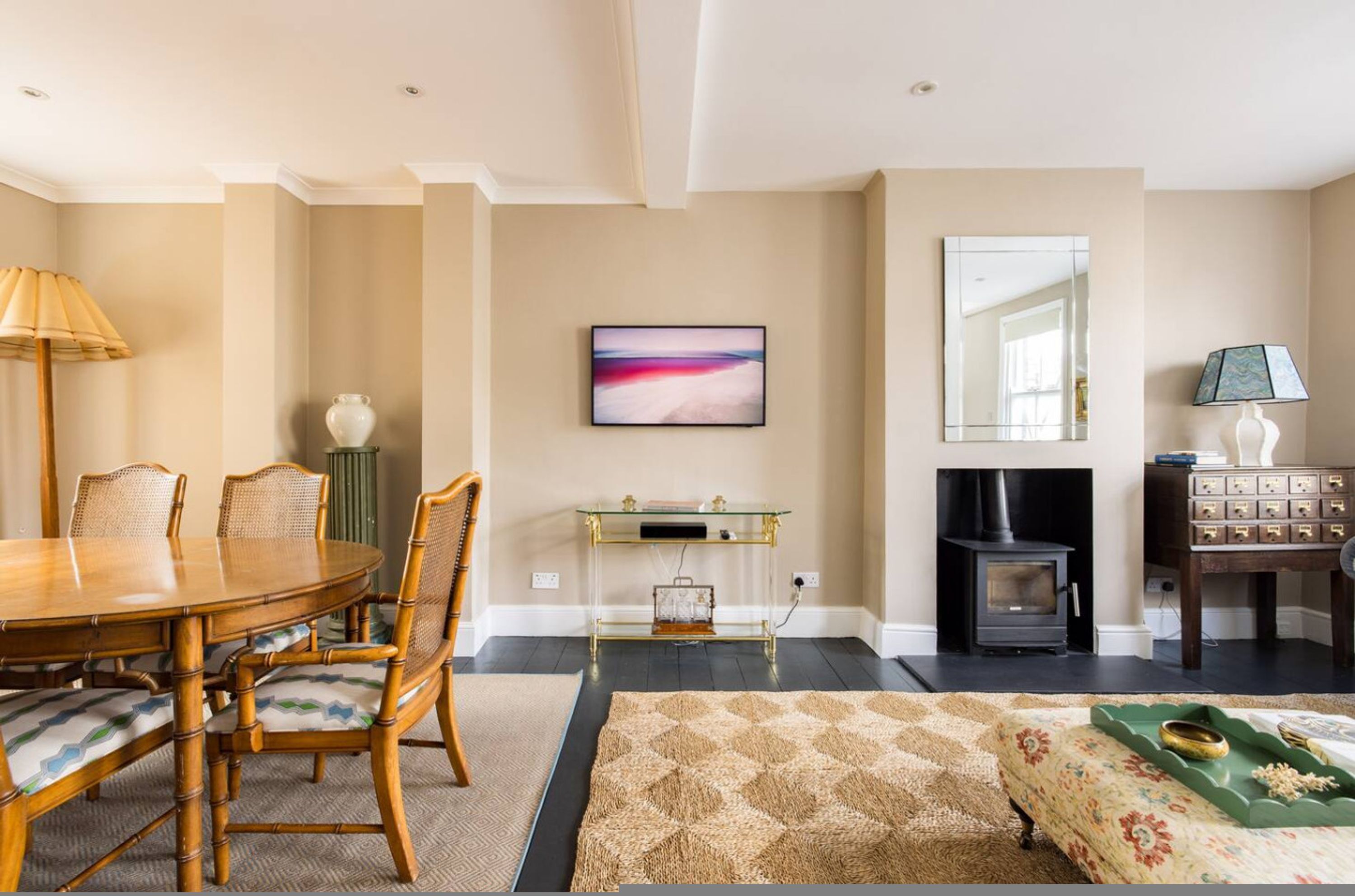 A living room with a round wooden dining table, wicker chairs, a glass console table, a fireplace, a television, and a sofa.