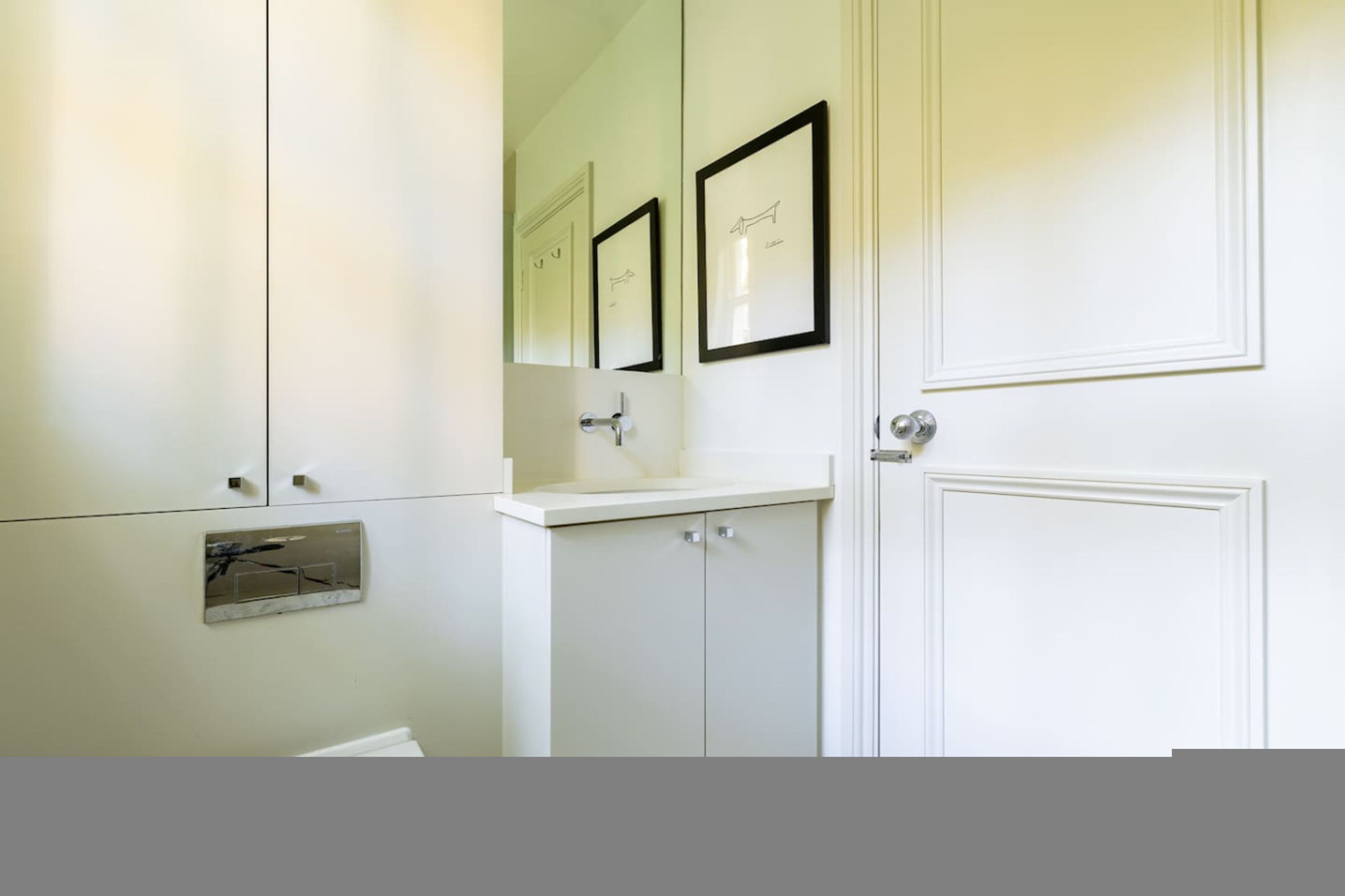 A bathroom with white cabinetry, a mirror, and framed pictures on the wall.
