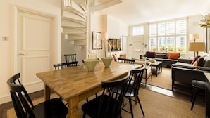 Ein Essbereich mit Wendeltreppe, ein Wohnzimmer mit Sofa und Couchtisch sowie ein Blick ins Freie durch große Fenster.