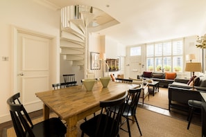 A dining area with a spiral staircase, a living room with a sofa and a coffee table, and a view of the outside through large windows. - Cobbled Charm 3 Bedroom House (London)