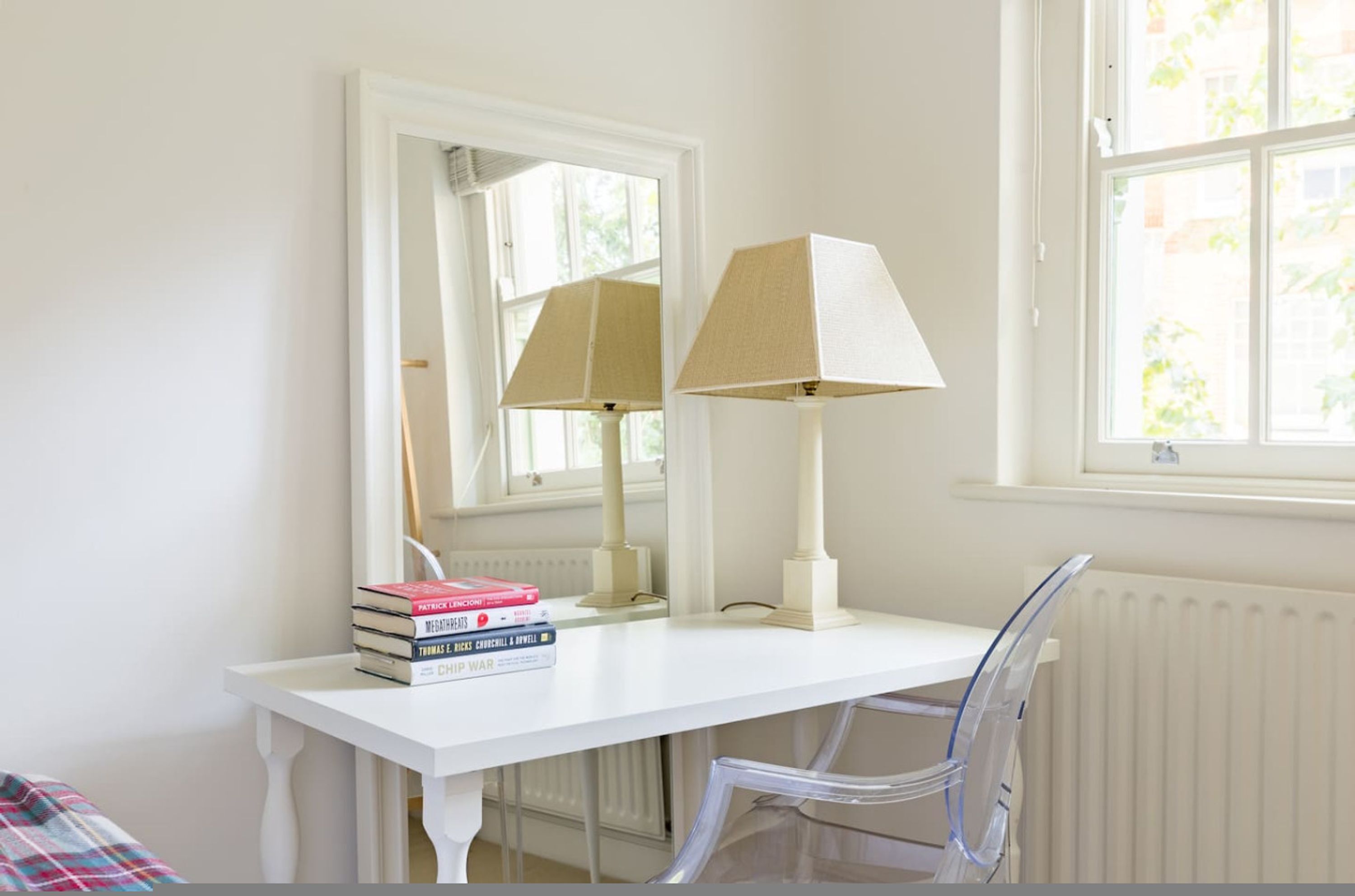 Un bureau blanc avec une lampe, une chaise et une pile de livres.