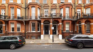 A row of red brick townhouses with black railings, numbered doors, and a street in front. - London Lovers - Newly Refurbished 2 BR in Chelsea (London)