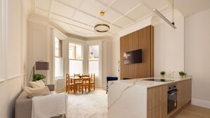 A modern kitchen with a built-in oven, a dining area with a table and chairs, and a living space with a sofa and a lamp. - London Lovers - Newly Refurbished 2 BR in Chelsea (London)