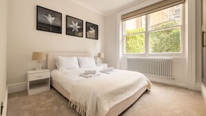 A bedroom with a bed, nightstands, a window with a view, and wall art. - London Lovers - Newly Refurbished 2 BR in Chelsea (London)
