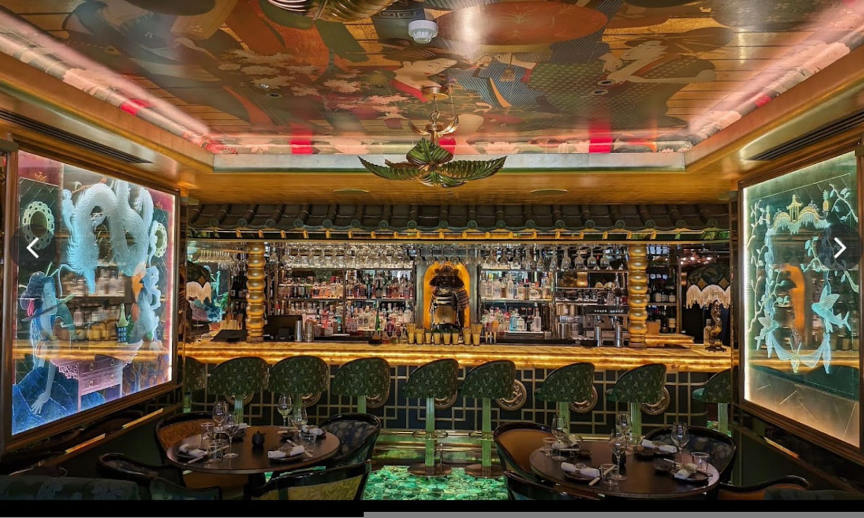 Un bar au décor d’inspiration asiatique traditionnelle, avec une statue de dragon au centre, des meubles en bois et un plafond orné de motifs complexes.