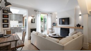 A modern living room with a sofa, a fireplace, a TV, and a dining area with a table and chairs. - Retreat to a Stylish 1 Bedroom Flat in Chelsea (London)