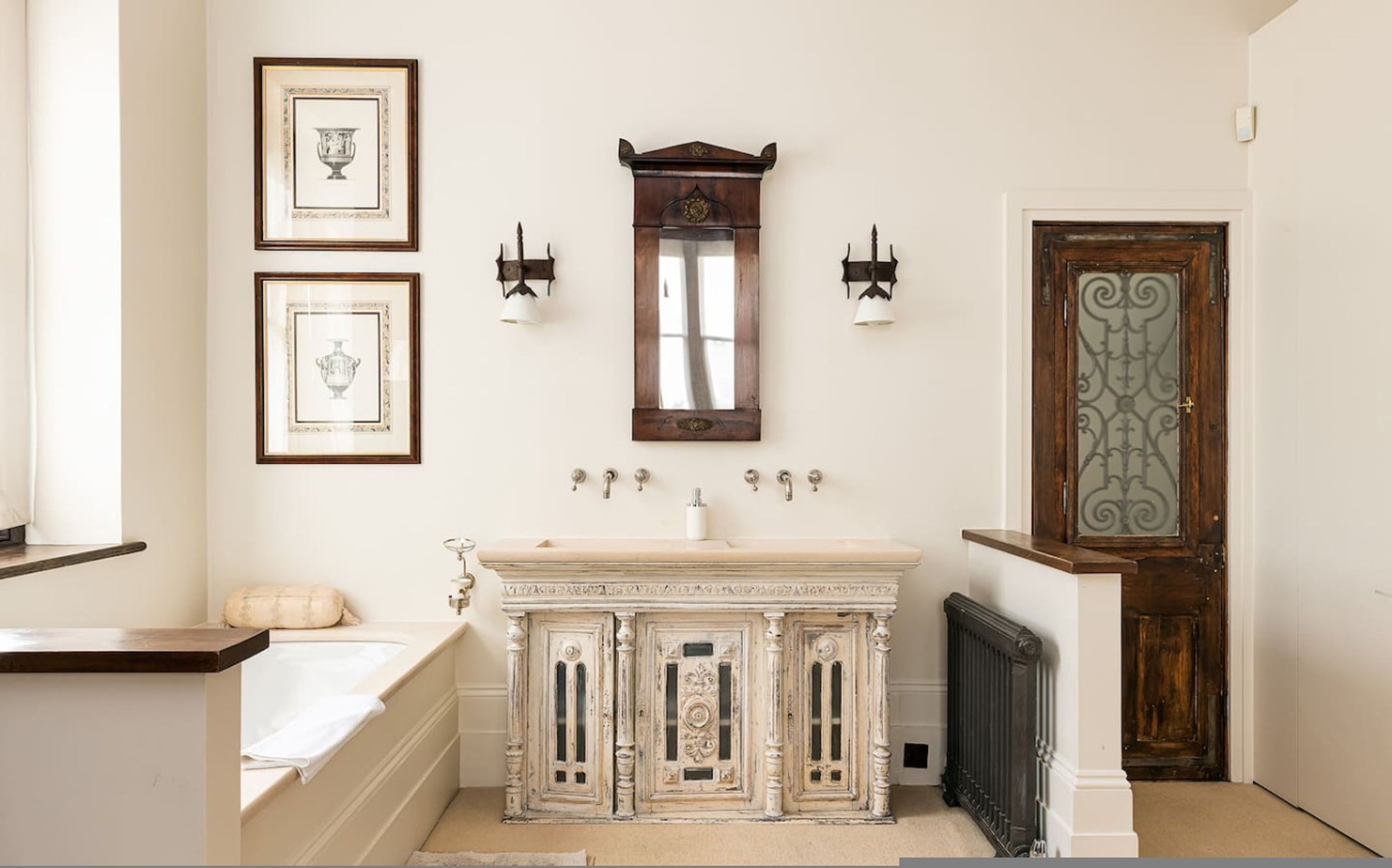 A bathroom with a bathtub, a sink with ornate cabinetry, and a large mirror.
