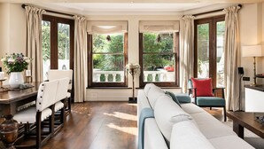 Ein Zimmer mit Esstisch, Stühlen, einer Couch und großen Fenstern mit Vorhängen.