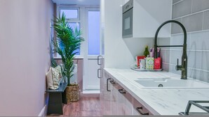 A modern kitchen with a white countertop, a black faucet, and a window with a view. - Clapham Calm 2 Bedroom Flat With Garden (London)