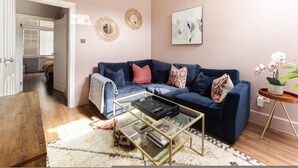 A living room with a blue sofa, a glass coffee table, and a small side table with a plant. - Clapham Calm 2 Bedroom Flat With Garden (London)