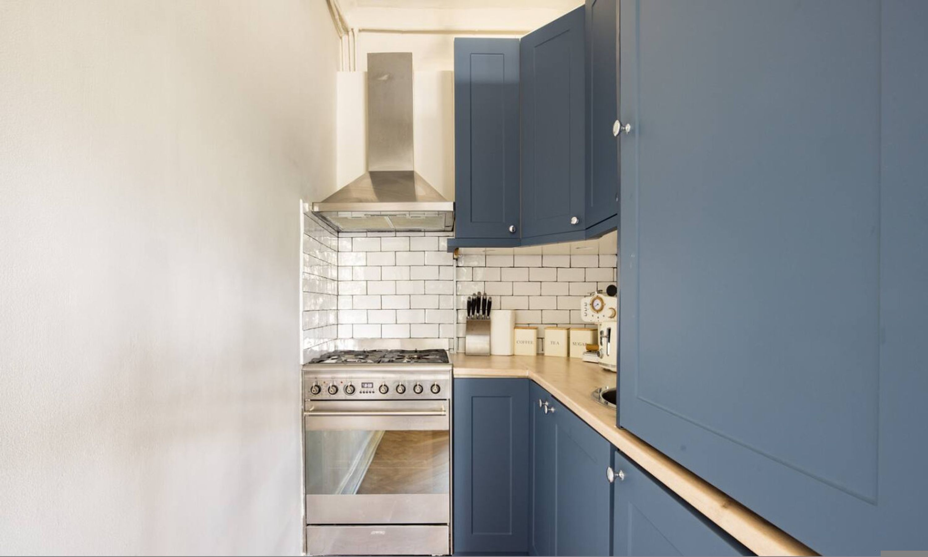 Une cuisine de taille réduite, dotée d’une cuisinière à gaz, d’un dosseret de carreaux blancs et de meubles bleus.