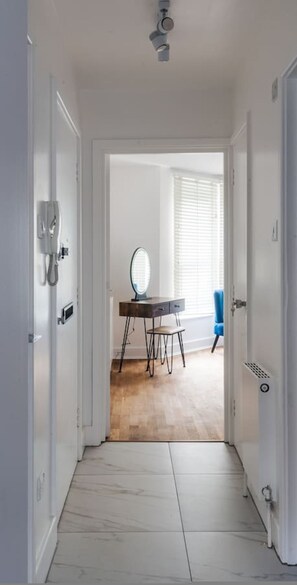 A hallway leading to a room with a desk, a mirror, and a window with blinds. - Stylish 1 BD in Notting Hill (London)