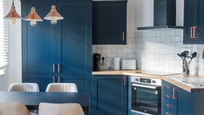 A kitchen with dark blue cabinets, a built-in oven, a coffee maker, and a toaster. - Stylish 1 BD in Notting Hill (London)