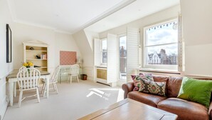 Una habitación con una mesa de comedor, sillas, un sofá, una mesa de centro, un radiador y una ventana con vistas a la ciudad.