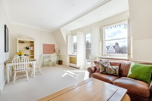 Ein Zimmer mit Esstisch, Stühlen, einer Couch, einem Couchtisch, einem Heizkörper und einem Fenster mit Blick auf die Stadt.