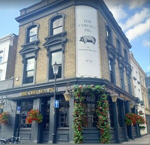 Ein Eckgebäude mit einem Schild, auf dem 'The Chelsea Pig' steht, und einem großen Banner mit einer Schweine-Illustration.