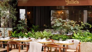 Un espace extérieur aménagé avec des tables et des chaises, un auvent portant l’inscription « Julie’s », et une végétation luxuriante.