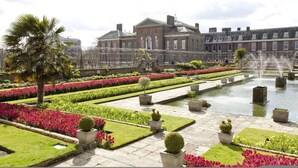 Un jardin à la française, agrémenté d’une fontaine, de haies soigneusement taillées et d’un grand bâtiment en arrière-plan.