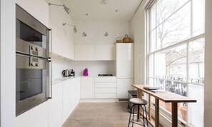 Eine moderne Küche mit weißen Schränken, einem eingebauten Backofen und einem Fenster mit Blick auf einen Balkon.