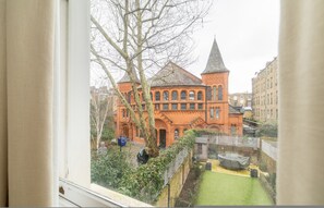 A view of a building with a large window, a tree in the foreground, and a fenced yard. - The Neutral Nest 1 BR in the Heart of Notting Hill (London)