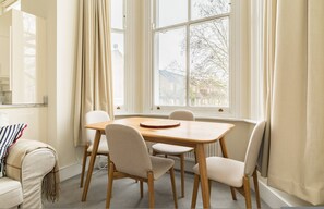 A room with a dining table, four chairs, a window with curtains, and a radiator. - The Neutral Nest 1 BR in the Heart of Notting Hill (London)