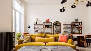 Ein Wohnzimmer mit einem gelben Sofa, einem Esstisch und einem großen Spiegel.