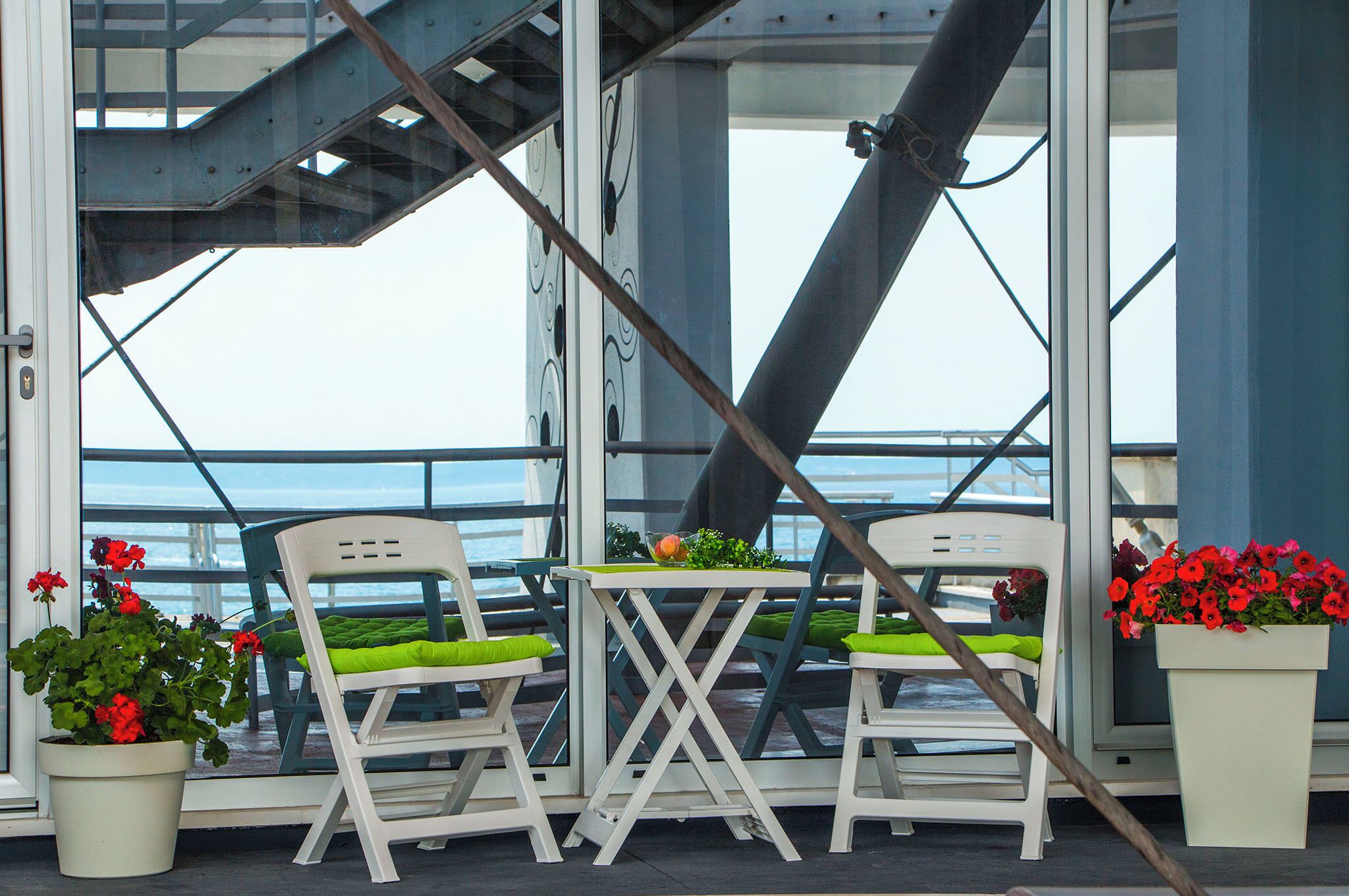 Ein Balkon mit zwei weißen Stühlen und einem kleinen Tisch, mit Blick auf ein Gewässer.