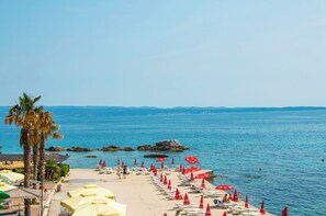 A beach with rows of sunbeds and umbrellas, a palm tree, and a view of the sea. - Idro apartments directly at the beach (Split)