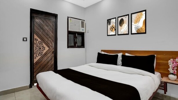 A bedroom with a bed, a wooden door, an air conditioning unit, and three framed artworks on the wall.