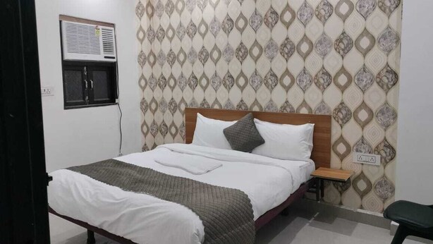 A neatly made bed with a wooden headboard, a bedside table, and a wall-mounted air conditioning unit.