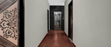 A hallway with a herringbone floor, a patterned wall on the left, and a door with a glass panel at the end.