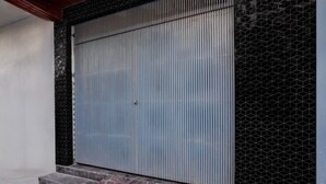 A closed metal door with vertical ridges, flanked by a patterned wall and a stone base.