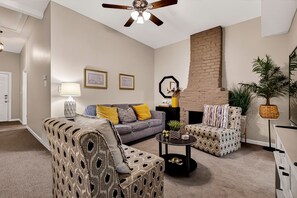 Ein Wohnzimmer mit grauem Sofa, gemusterten Sesseln, einem Couchtisch und einem Kamin.
