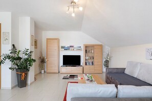 Ein modernes Wohnzimmer mit Flachbildfernseher, Holzschränken, einer Couch und einem Blumentopf.